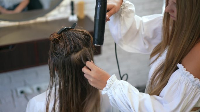缓慢的运动。在美发沙龙里，一位女理发师正在用吹风机给坐在椅子上的顾客吹湿头发。