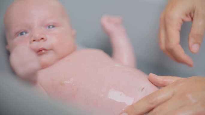 在家里的浴缸里，妈妈的手把水滴在男婴的肚子上