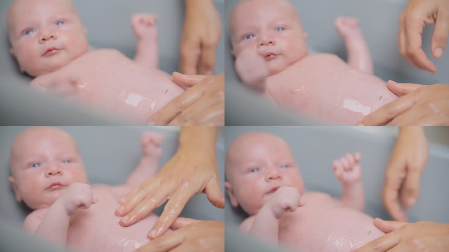 在家里的浴缸里，妈妈的手把水滴在男婴的肚子上