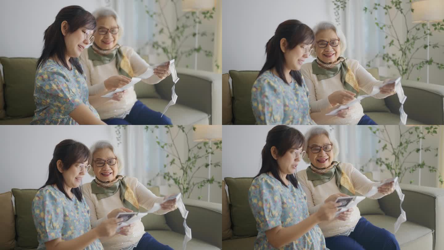 一位快乐的孕妇和她的祖母坐在家里客厅的沙发上，展示着未出生婴儿的超声波扫描。