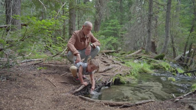 好奇的小女孩和爷爷在溪边的大自然中玩耍