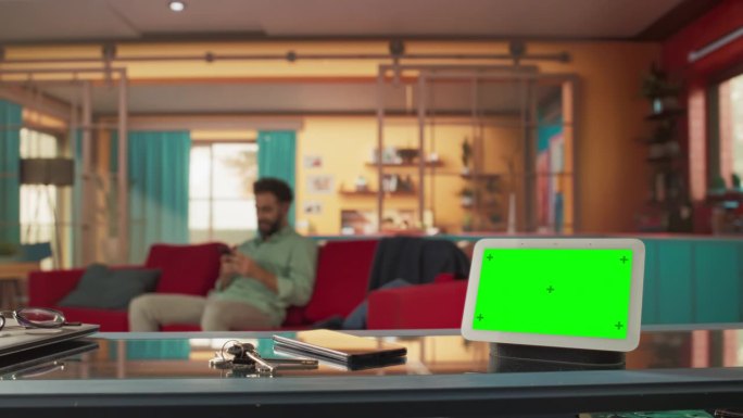 创意智能家居设备与绿色屏幕显示。在后台的人使用智能手机来控制他的时尚家居环境。物联网高科技无线智能系