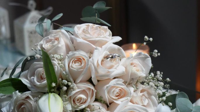 白色的金戒指镶嵌在新娘捧花的白色玫瑰花瓣之间。婚礼的细节