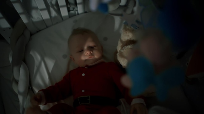 正上方是穿着圣诞老人服装的顽皮男孩躺在家里的婴儿床上的肖像