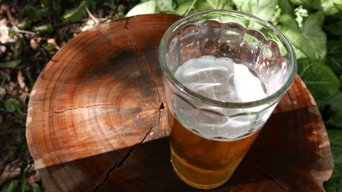 POV:某人在观察桌子上的一杯啤酒。在随意的阳光下喝一杯啤酒。在户外喝杯啤酒。一杯啤酒，俯视图。喝啤