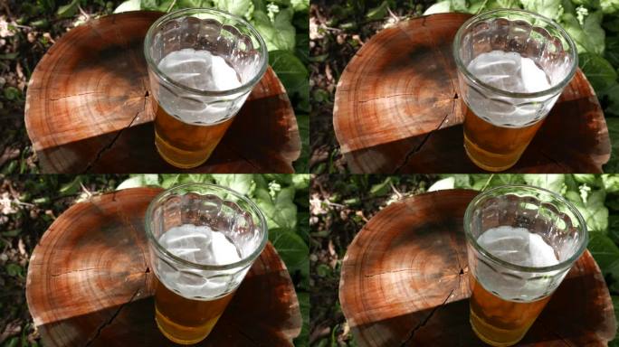 POV:某人在观察桌子上的一杯啤酒。在随意的阳光下喝一杯啤酒。在户外喝杯啤酒。一杯啤酒，俯视图。喝啤