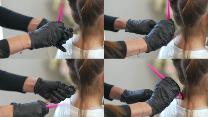 理发师戴着橡胶手套，手里拿着一缕女孩的头发，用梳子把它梳理起来涂上颜料。