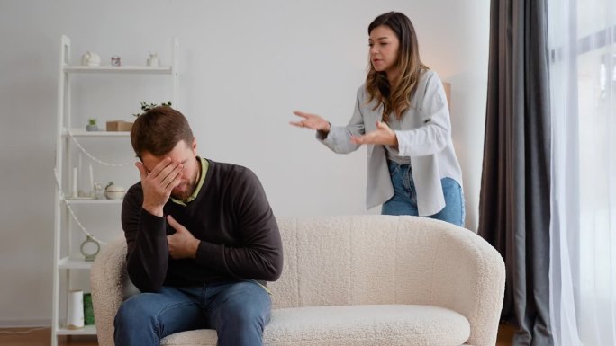 好斗的女人在家里对害怕的丈夫大吼大叫。一个男人抱着自己的胸膛，感到心痛