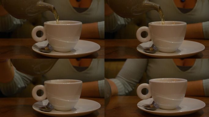 特写:一位女士用手把传统的英国茶从茶壶里倒进白色的杯子里