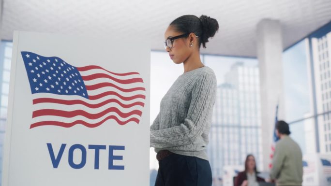 年轻时尚的非裔美国女性在投票站投票，并把选票放进密封的盒子里。美国人民在选举日在美利坚合众国