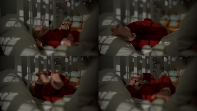 白天在暗房里，穿着圣诞老人服装的小男孩躺在婴儿床上打哈欠的手持照片