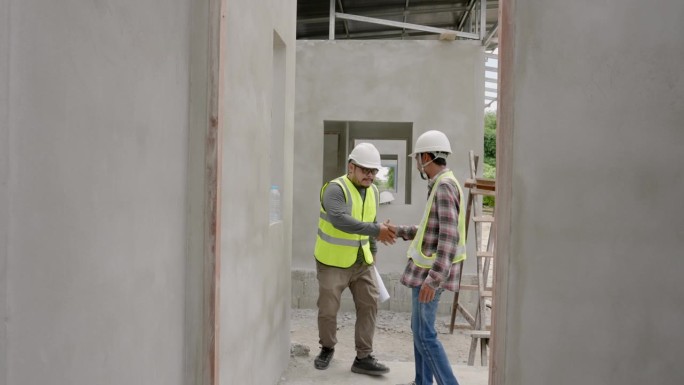 两名男建筑工程师曾在一起工作，走进去互相认识，使他们的工作在一起工作时更容易，两人戴着安全帽反光安全