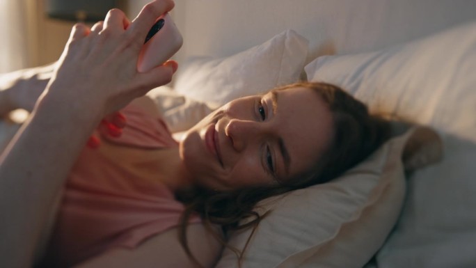 快乐女孩在床上看智能手机屏幕的特写。困倦的女人读留言