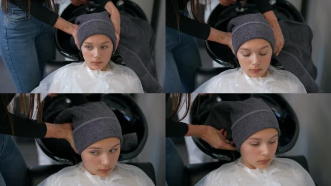 一位女理发师用毛巾擦干一个女孩的头发，把它缠在她的头上。女孩躺在理发师的椅子和水槽。