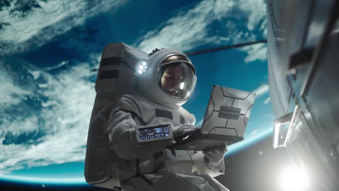 一个年轻的宇航员在外太空失重漂浮的肖像。宇航员在轨道飞船外用笔记本电脑工作。男子正在上网，正在连接卫