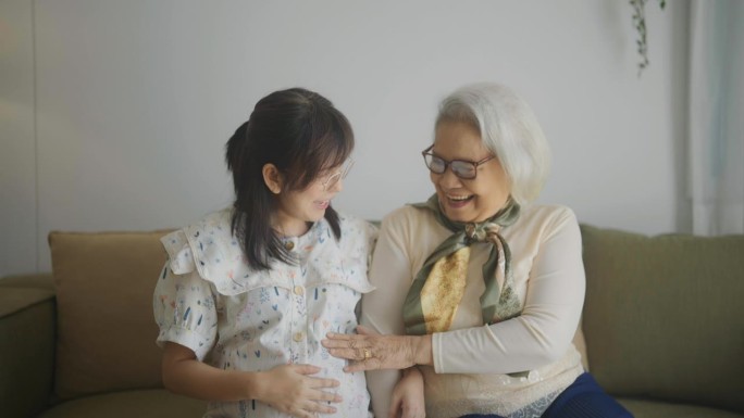 兴奋的老妇人抚摸着怀孕的女儿的肚子，微笑着与女儿在客厅度过时光