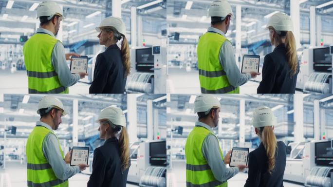 现代电子厂自动装配线上，白人男性工艺工程师用平板电脑与女主管交谈。同事们戴着安全帽，讨论新的复杂项目