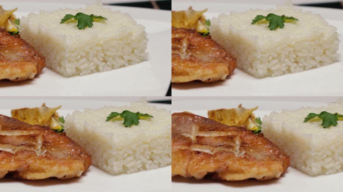 白盘子里的一块煎鱼，配上煮熟的米饭和柠檬。餐馆里供应鱼的。特写镜头，水平镜头移动