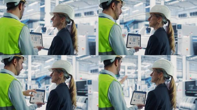 在电子厂的自动装配线上，白人男性工程师使用平板电脑与女性工业技术人员交谈。同事们戴着安全帽，讨论新产