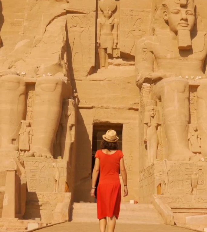 在埃及南部努比亚的纳赛尔湖畔，一名身穿红色连衣裙的年轻女子走向纳菲尔塔里神庙，神庙旁边是阿布辛贝神庙