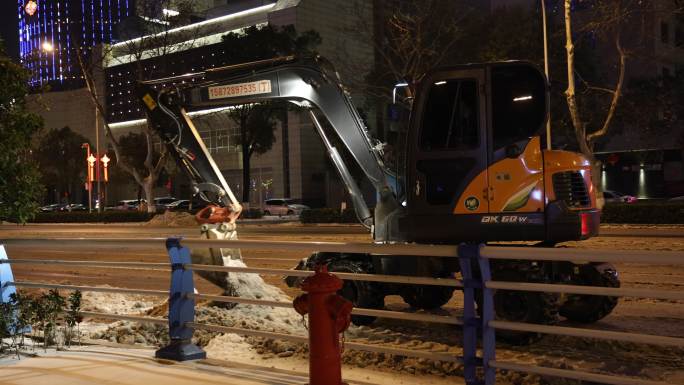 夜晚挖机在道路上除雪除冰