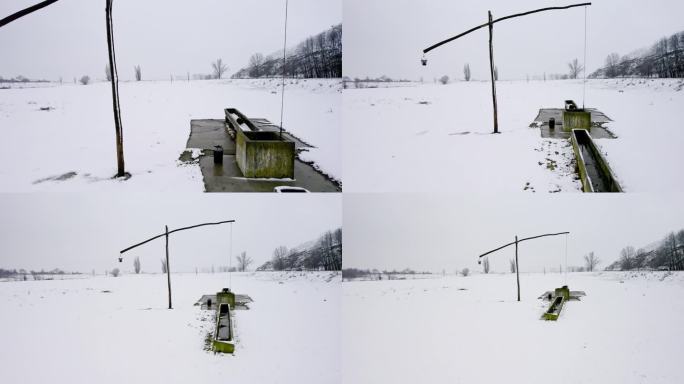 无人机在积雪覆盖的土地上捕捉到带桶的旧木制水井泵