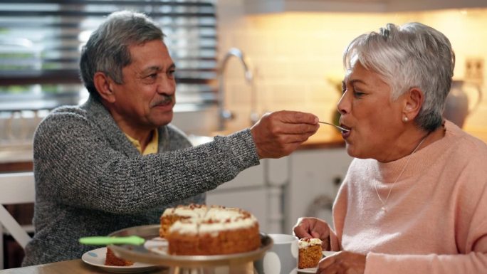 爱情，蛋糕和老两口在厨房一起吃茶点，在家里团聚。快乐，浪漫，退休老人在家里的餐桌上给他的妻子吃甜点。