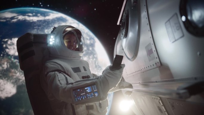 年轻的宇航员漂浮在零重力的太空中。宇航员在轨道航天器外的开放空间使用智能手机，浏览互联网内容，社交媒
