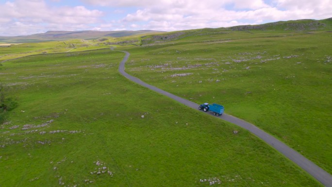 航拍:蓝色拖拉机满载着割过的草行驶在乡间小路上