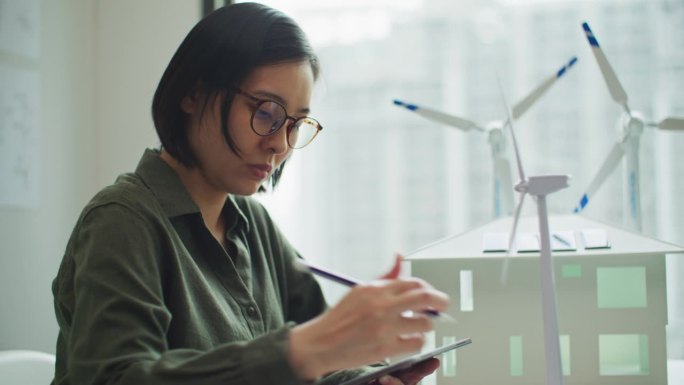 女工程师或发明家寻找风力发电机模型并在办公室使用平板电脑