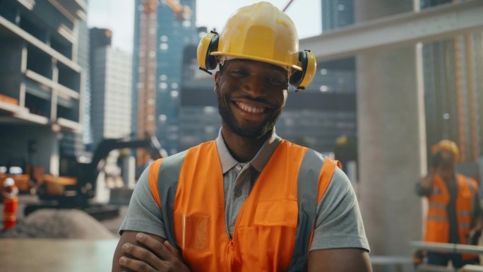 幸福成功的黑人建筑工人的肖像，双臂交叉站着，对着镜头摆姿势，微笑着。专业重工工程师，穿安全制服，戴安