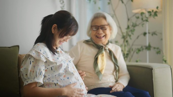 一位老妇人在家里亲切地抚摸着怀孕女儿的肚子。