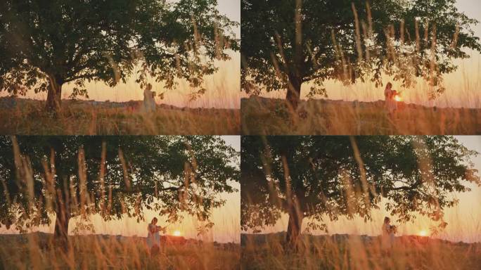 SLO跟踪拍摄的母亲抱着孩子在大树下，对着晴朗的天空在日落