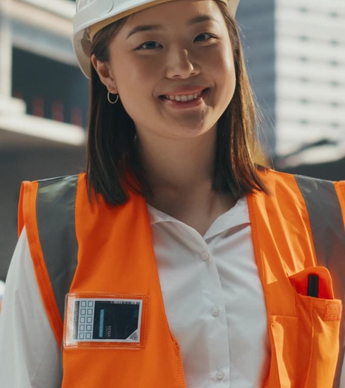 竖屏:在住宅建筑工地穿着安全制服和安全帽的重工业亚洲工程师。微笑的日本女工业现场经理站在户外