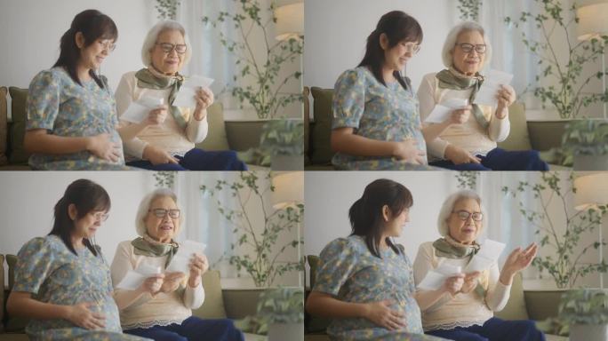 快乐的年轻孕妇向坐在客厅沙发上的母亲展示未来宝宝的超声波照片