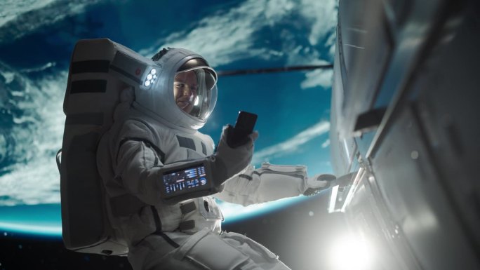 年轻的宇航员漂浮在零重力的太空中。宇航员在轨道航天器外的开放空间使用智能手机，与地球上的发射操作中心