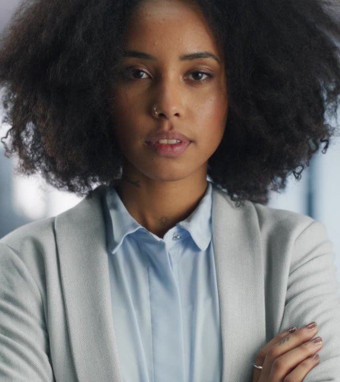 垂直屏幕:时尚的黑人女孩与非洲头发，鼻子穿孔和纹身在现代办公室摆姿势。漂亮的非洲员工看着镜头。年轻专