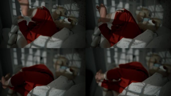 白天，穿着圣诞老人服装的顽皮小男孩躺在家里的婴儿床上的手持照片