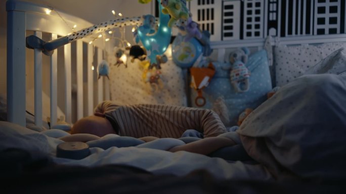 在家里的暗房里，顽皮的小男孩躺在婴儿床上的手持照片