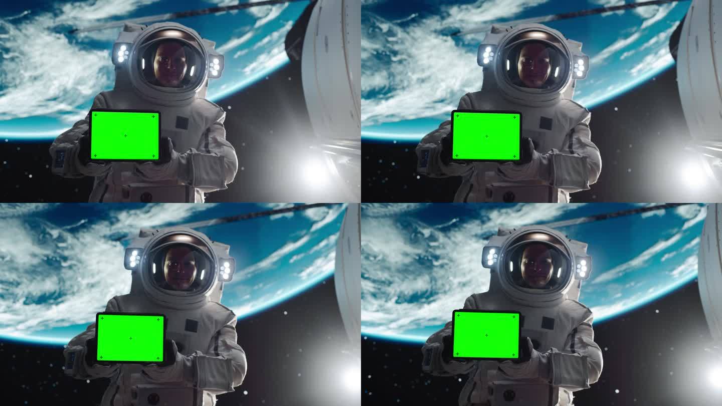 一个英俊的年轻宇航员手持平板电脑的肖像，绿色屏幕模板在水平位置。训练有素的专业人员穿着太空服为模拟广