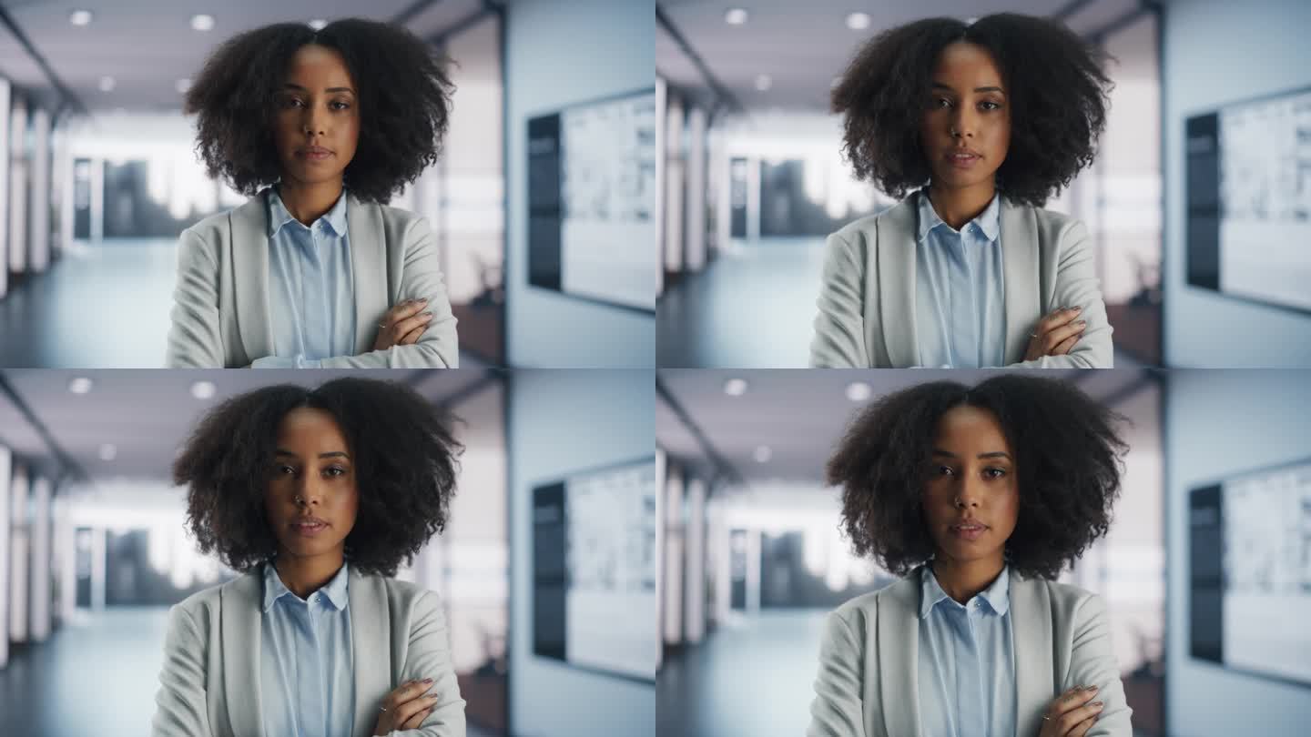 一位美丽的非裔美国女性在现代办公室走廊里摆造型的肖像。成功的年轻黑人女性双臂交叉站在镜头前
