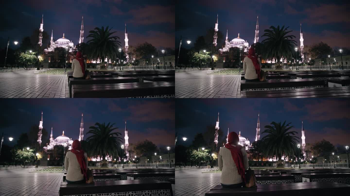 无法辨认的穆斯林妇女在灯火辉煌的广场上沉思圣索菲亚大教堂的雄伟之美#圣索菲亚之夜#宁静的反思#城市之
