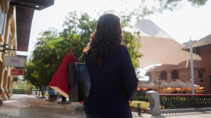 在一个阳光明媚的夏日，一个拎着购物袋的女人走在熙熙攘攘的城市街道上，周围的人，包括一个孩子和一对夫妇