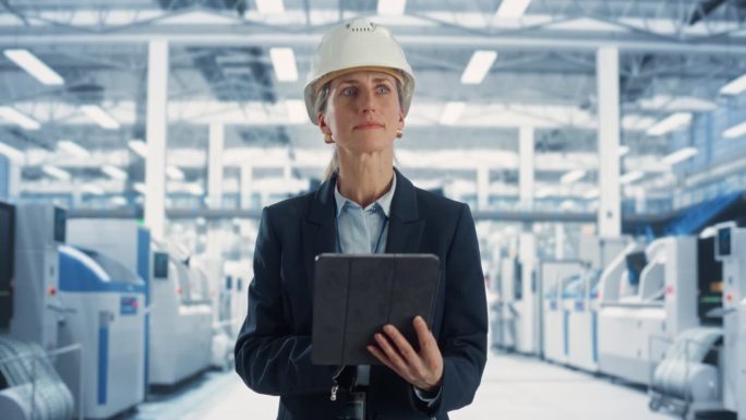 白人女工程师站在工厂大厅，使用平板电脑在机械制造设施的肖像。专家使用在线软件编程现代生产线