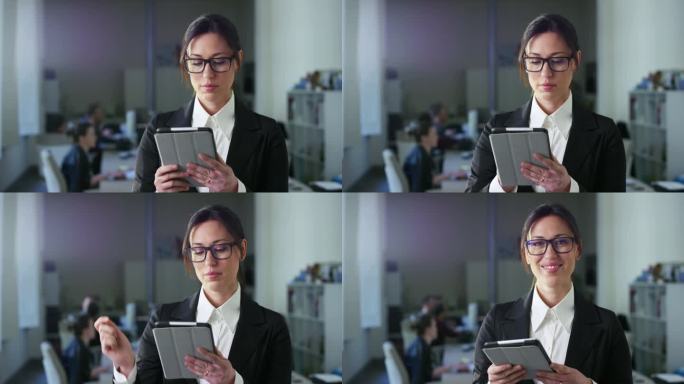 穿着正装，用平板电脑，站在现代多元化的办公室里处理金融、商业和营销项目的成功女商人肖像。她看着相机，
