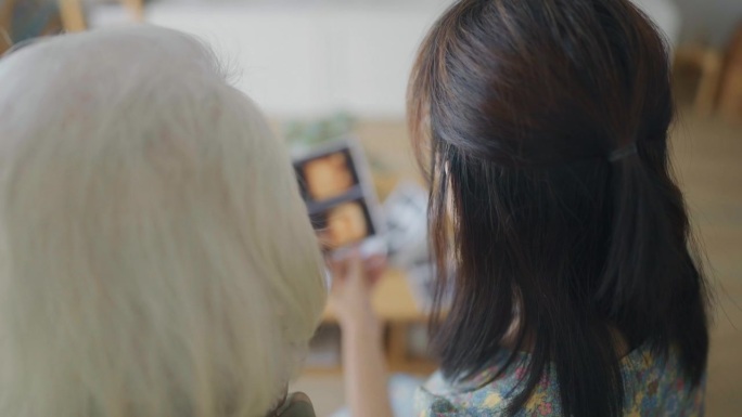 一名孕妇和她的祖母坐在家里展示她未出生的孩子的超声波照片。