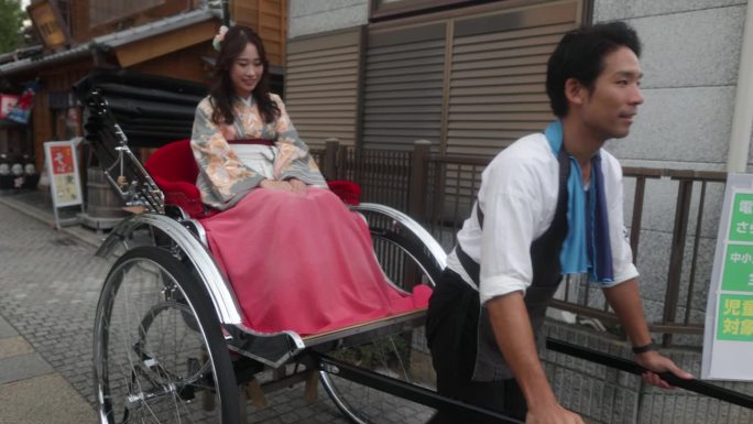 在传统的日本小镇上，穿着和服/袴的妇女在人力车上挥手