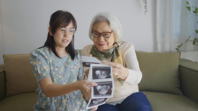 亚洲妇女和她的母亲度过美好的时刻在一起，他们分享爱的谈话，同时看着她的超声波扫描x射线婴儿出生在一起