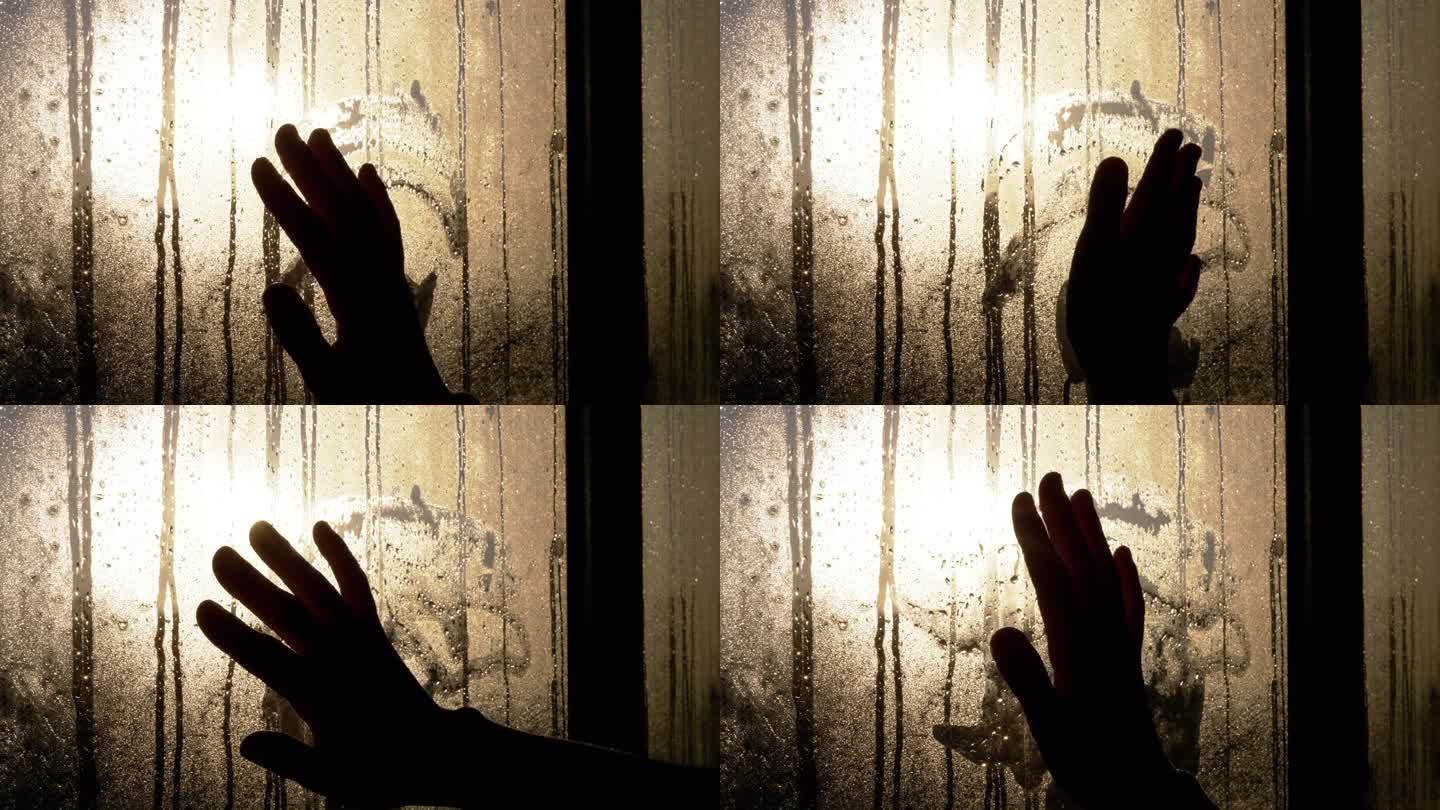 一个女人的手的剪影触摸雾蒙蒙的潮湿的窗户在闪烁的阳光眩光