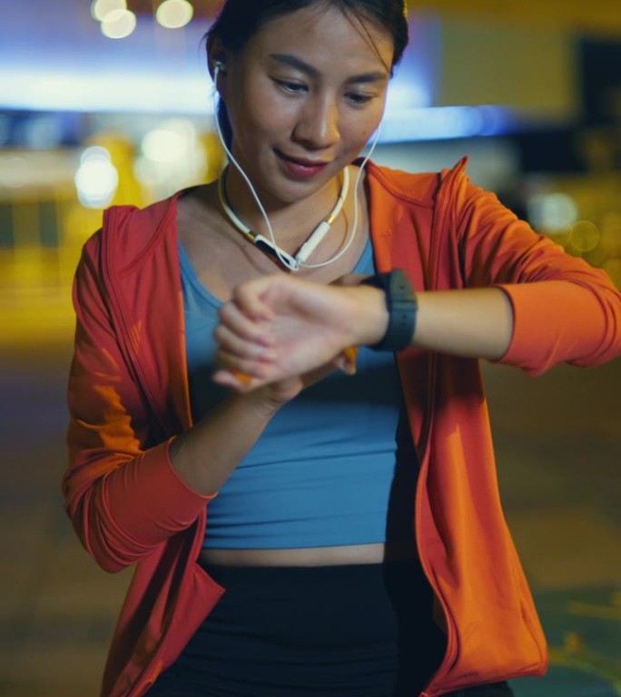 年轻的亚洲女运动员跑步者在城市夜间户外跑步前检查智能手表和心率监测器的进度。健康的锻炼。垂直的屏幕。